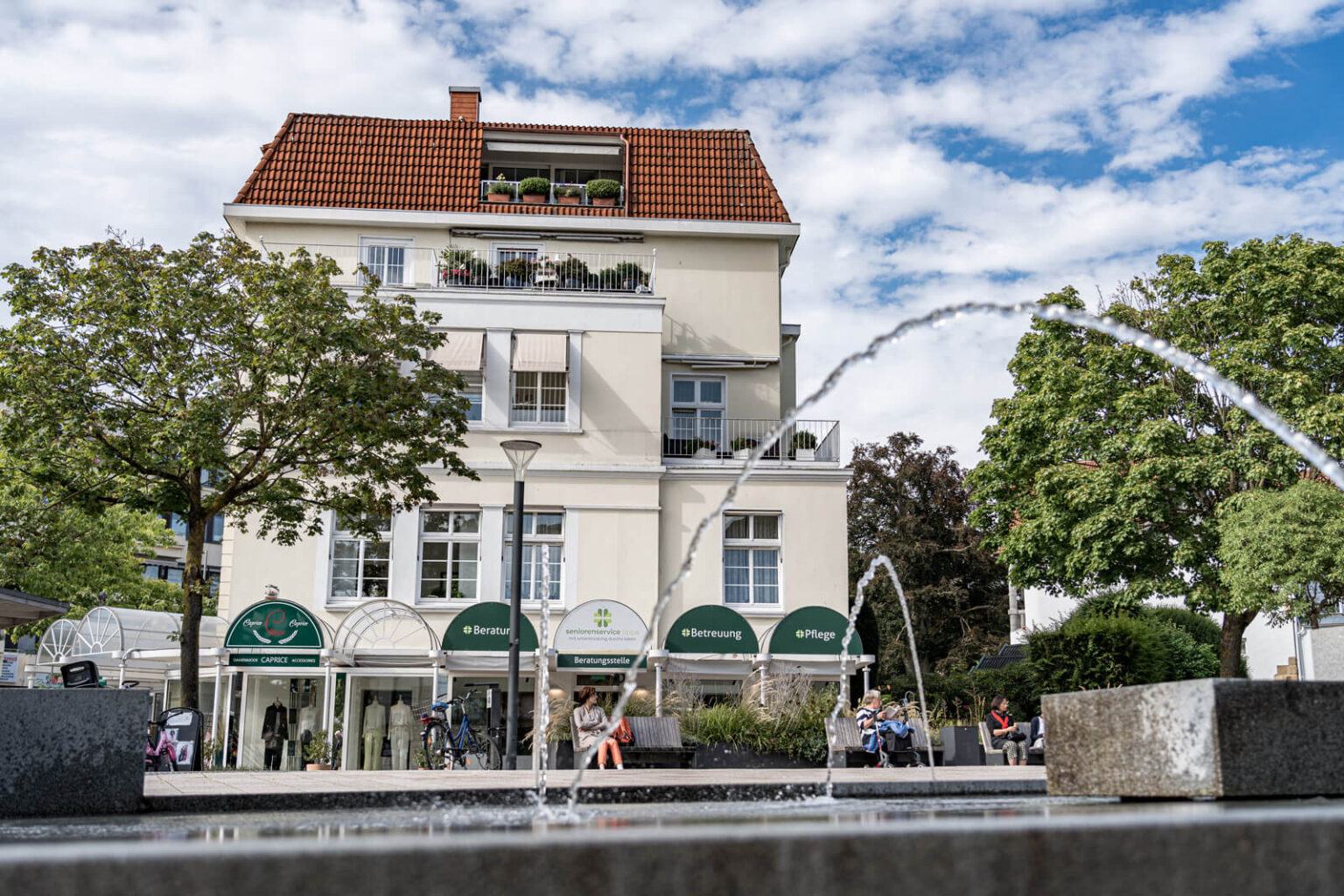Gebäude mit Arkaden vor einer Wasserfontäne